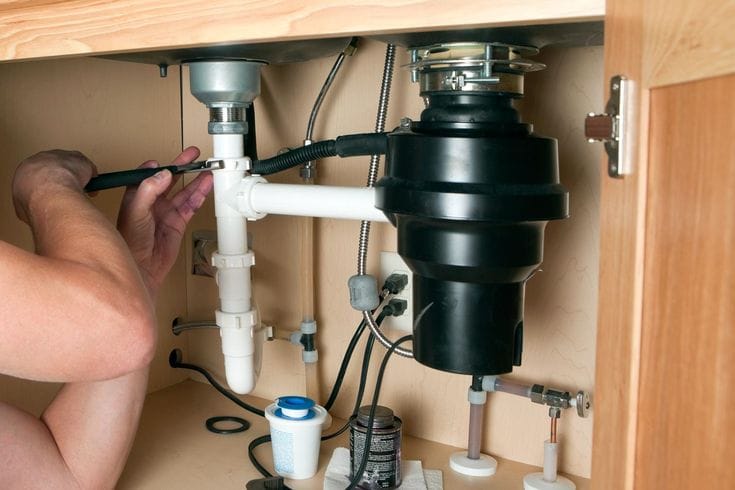 Plumber installing a garbage disposal beneath a kitchen sink in Jacksonville
